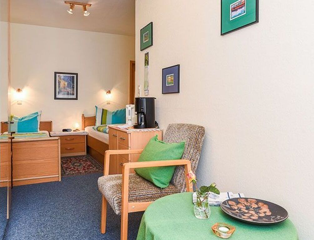 A hotel room with a bed, a desk, a chair, a coffee machine, and framed pictures on the wall.
