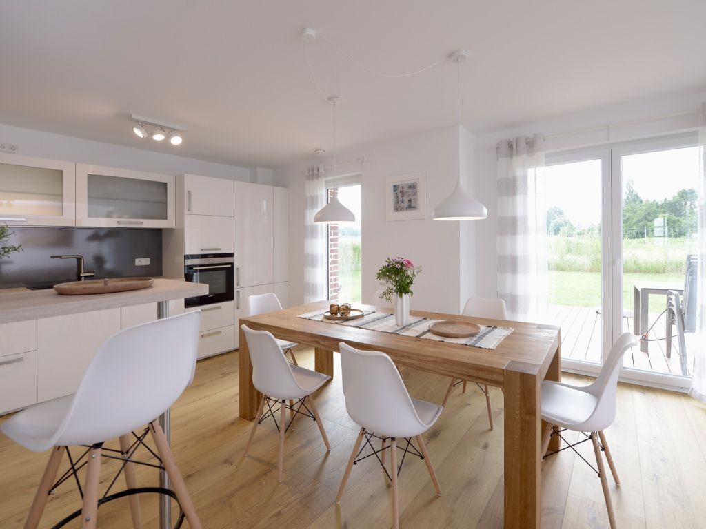 A modern kitchen with white cabinetry, a wooden dining table, and white chairs.