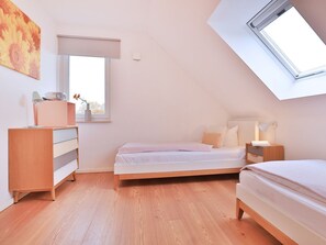 A bedroom with a skylight, a bed, a nightstand, a dresser, and a window.