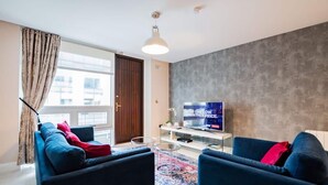 Un saló modern amb un sofà, una televisió plana i una finestra gran amb cortines.