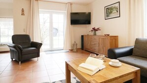 A living room with a sofa, a coffee table with a book and a cup, a TV mounted on the wall, and a cabinet with decorative items. - Sonnenblick holiday house (Kalkhorst)