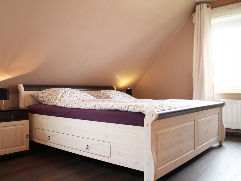 Una cama individual con estructura de madera, una mesita de noche con lámpara y una ventana con cortinas.