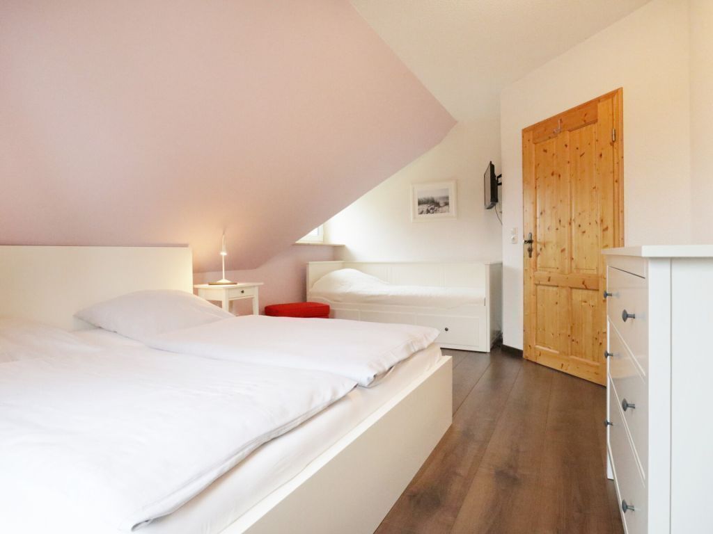 Une chambre à coucher comprenant un lit, une table de chevet, une commode, une porte en bois et une petite table avec une lampe.