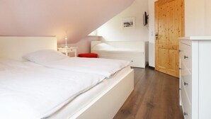 A bedroom with a bed, a nightstand, a dresser, a wooden door, and a small table with a lamp. - Sonnenblick holiday house (Kalkhorst)