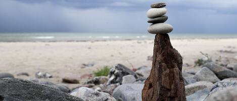 Un montón de piedras equilibrado sobre un tocón de árbol en una playa rocosa, con un cielo nublado al fondo.