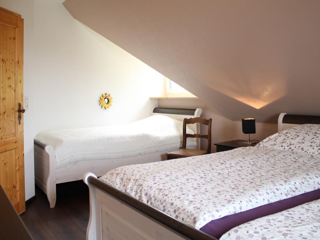 Une chambre avec deux lits, une porte en bois, une petite table, une chaise et une étagère fixée au mur.