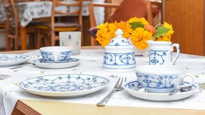 Une table à manger dressée avec de la vaisselle bleue et blanche à motifs, un vase contenant des fleurs jaunes et, au fond, une chaise en bois.