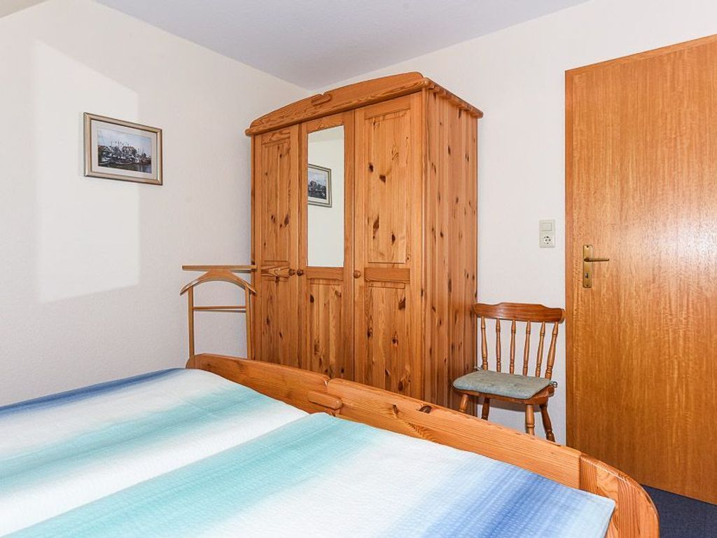 Un dormitorio con cama, armario de madera, silla y una puerta.