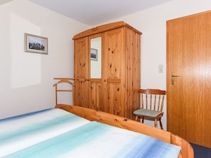 Quarto com cama, guarda-roupa de madeira, cadeira e porta.
