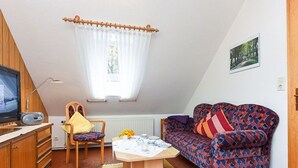 Un salon chaleureux avec un téléviseur, un canapé à motifs, une chaise en bois et une table à manger.