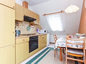 Uma cozinha compacta com armários de madeira, micro-ondas, fogão e um espaço de jantar com mesa e cadeiras.
