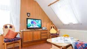 Une pièce chaleureuse, dotée d’un téléviseur, de meubles en bois, d’une table à manger et d’un plafond en pente.