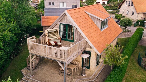 Ein zweistöckiges Haus mit Balkon, einer Holzterrasse und einer kleinen Patio.