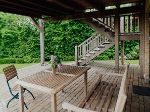 A wooden deck with a table and chairs, a wooden staircase, and a garden in the background. - Traveblick, Germany (Kalkhorst)