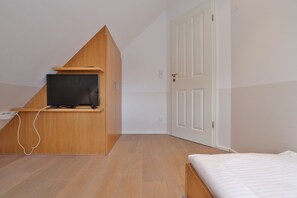 A bedroom with a bed, a TV mounted on a wooden shelf, a white door, and a light switch. - Traveblick, Germany (Kalkhorst)