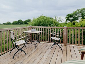 A wooden deck with two metal chairs and a small table, surrounded by a wooden railing. - Traveblick, Germany (Kalkhorst)