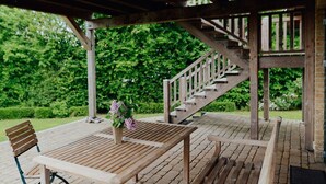 Eine Holzterrasse mit Tisch und Stühlen, eine Holztreppe und ein Garten im Hintergrund.