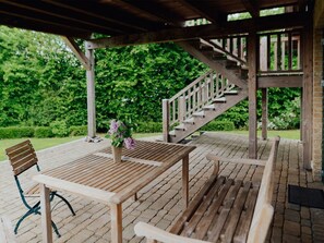A wooden deck with a table and chairs, a wooden staircase, and a garden in the background.