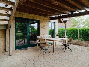 An outdoor patio with a wooden table and chairs, a green door, and a brick wall. - Traveblick, Germany (Kalkhorst)