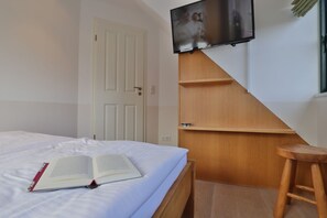 A bedroom with a bed, a book, a TV mounted on the wall, a wooden staircase, and a door.