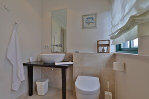 A bathroom with a white sink, a toilet, a mirror, and a window with a view.