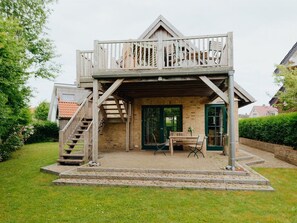 A two-story wooden house with a balcony, a staircase leading to the upper floor, and a small outdoor seating area with a bench and table. - Traveblick, Germany (Kalkhorst)