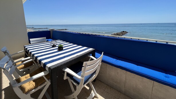 Een balkon met een tafel en stoelen, met uitzicht op zee.