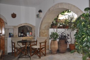 An outdoor patio with a stone table and chairs, surrounded by large potted plants and a stone archway.
