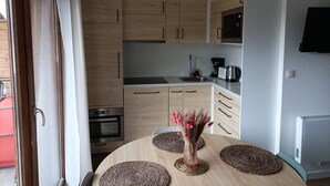 Una cocina moderna con armarios de madera, horno empotrado, lavaplatos y microondas. Hay una mesa de comedor con individuales tejidos y un jarrón con flores.