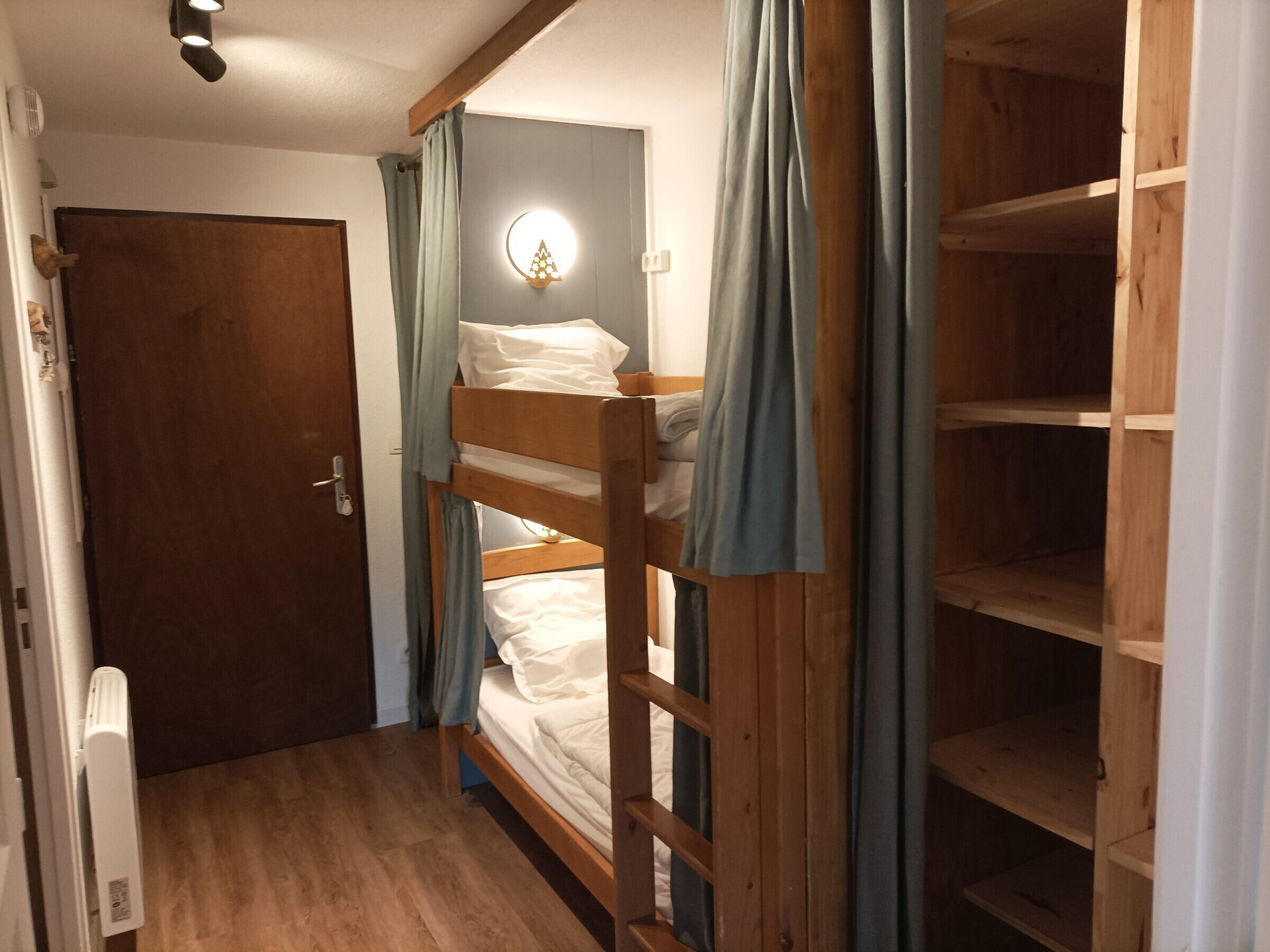 A bunk bed room with a wooden door, a wall-mounted light, and a wooden shelf unit.