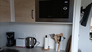 Una cocina moderna con microondas de acero inoxidable, cafetera, tostadora y hervidor. Hay armarios de madera y una encimera blanca.