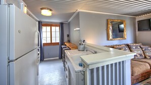 Cocina pequeña con refrigerador, pileta y encimera de madera. En la zona de estar, un sofá con cojines estampados.