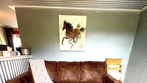 Un sofá de cuero marrón con un cojín estampado, un cuadro de caballos en la pared y una alfombra multicolora en el suelo.
