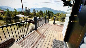 Una terraza de madera con barandilla metálica, con vistas a un paisaje montañoso.