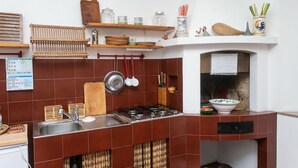 Una cucina con piano cottura a gas, lavello e diversi utensili. Si vedono scaffali con barattoli e un gallo decorativo.