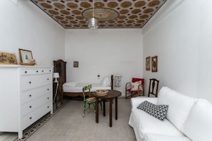 A room with a bed, a white sofa, a wooden dresser, a chair, a small table, and a ceiling with a geometric pattern. - S190 - Sirolo, three-room apartment in the square (Sirolo)