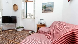 Una stanza con televisore, radio, tappeto a motivi, letto con copriletto a righe, finestra vista e un quadro appeso al muro.