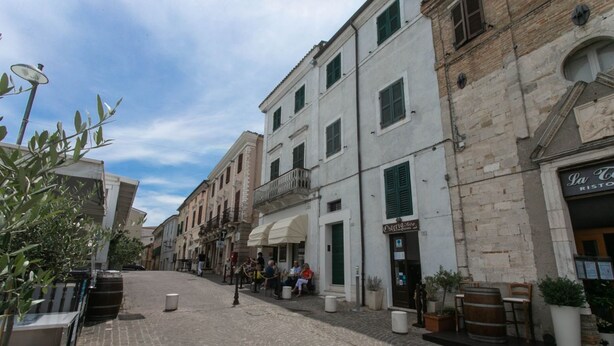 Una strada acciottolata con edifici, posti a sedere all'aperto e piante in vaso.