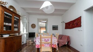 Un'area pranzo con un tavolo apparecchiato per quattro persone, un mobiletto in legno con stoviglie, un tappeto decorato e un arazzo rosso appeso al muro.