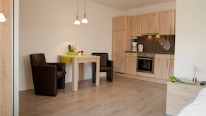 A modern kitchen with wooden cabinets, a dining table with chairs, and a coffee maker. - Apartment Alma - Apartment Lühe (Jork)
