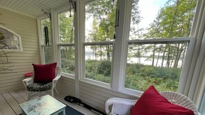 Eine gemütliche Veranda mit Korbmöbeln, einem kleinen Tisch und Blick auf einen See und Bäume.