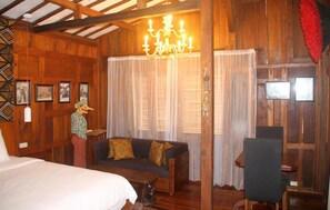 A wooden room with a bed, a sofa, a chandelier, and framed pictures on the wall.