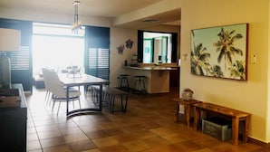 Een ruime woonkamer met een eettafel, stoelen, een bank en een keuken met een aanrecht en barkrukken.