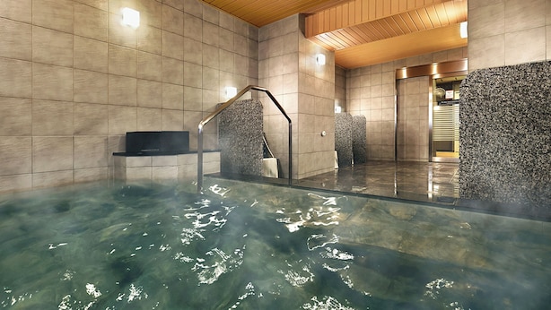 Een modern binnenzwembad met helder water, een houten plafond en betegelde wanden.
