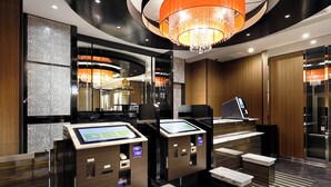 Een modern hotel ontvangstgedeelte met een digitale incheck kiosk, een kroonluchter en een spiegel die het interieur weerspiegelt.