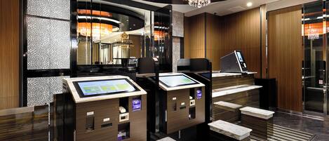 Een modern hotel ontvangstgedeelte met een digitale incheck kiosk, een kroonluchter en een spiegel die het interieur weerspiegelt.