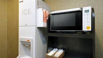 Habitación de hotel con dispensador de hielo blanco y microondas en un estante.