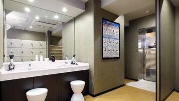 A modern bathroom with a large mirror, two sinks, and a toilet. There is a poster on the wall with safety instructions.