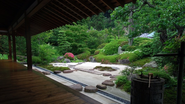 Un jardín japonés tradicional con un sendero de madera, rocas y abundante vegetación.
