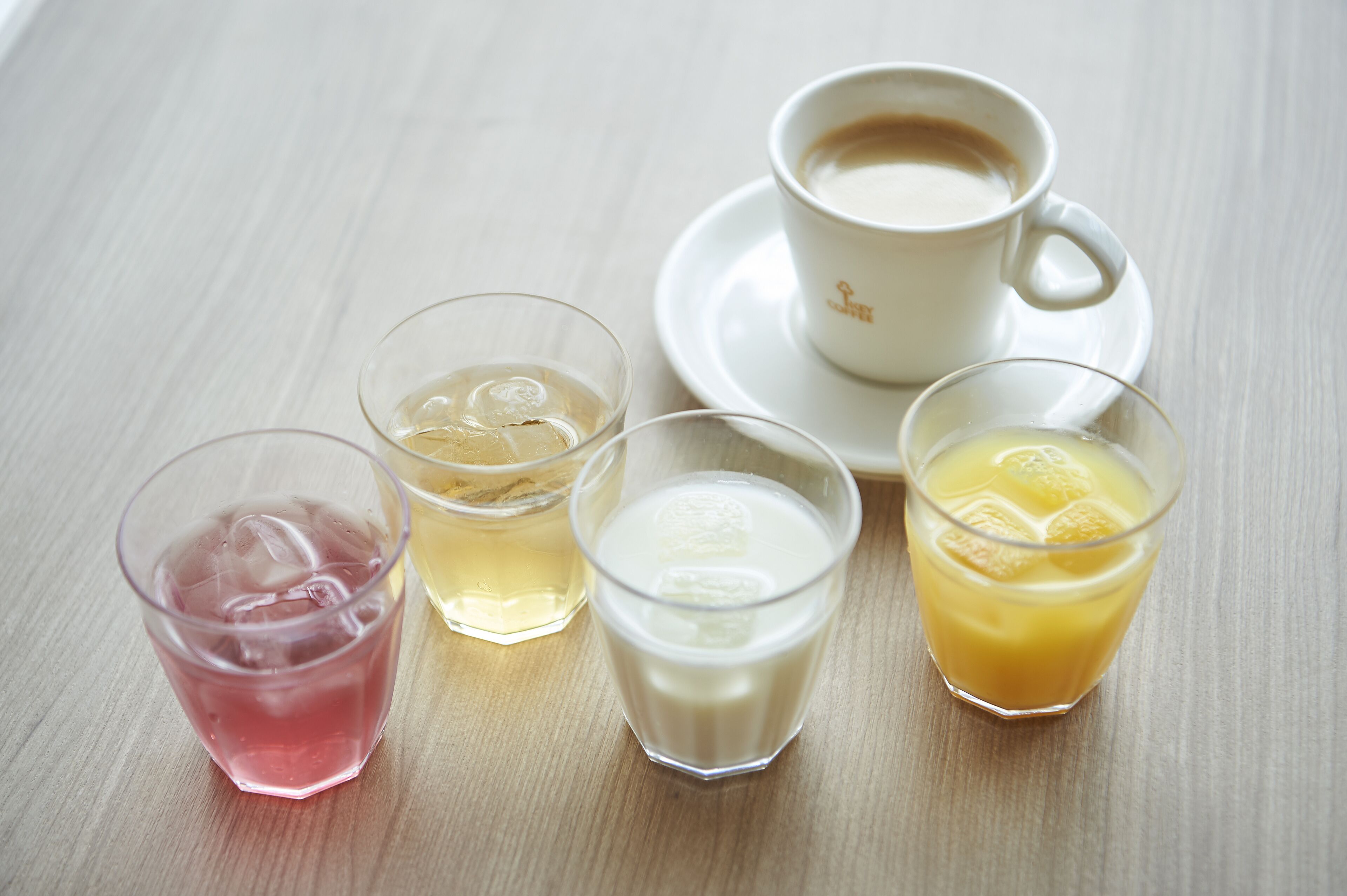 A table with four glasses of beverages and a cup of coffee.